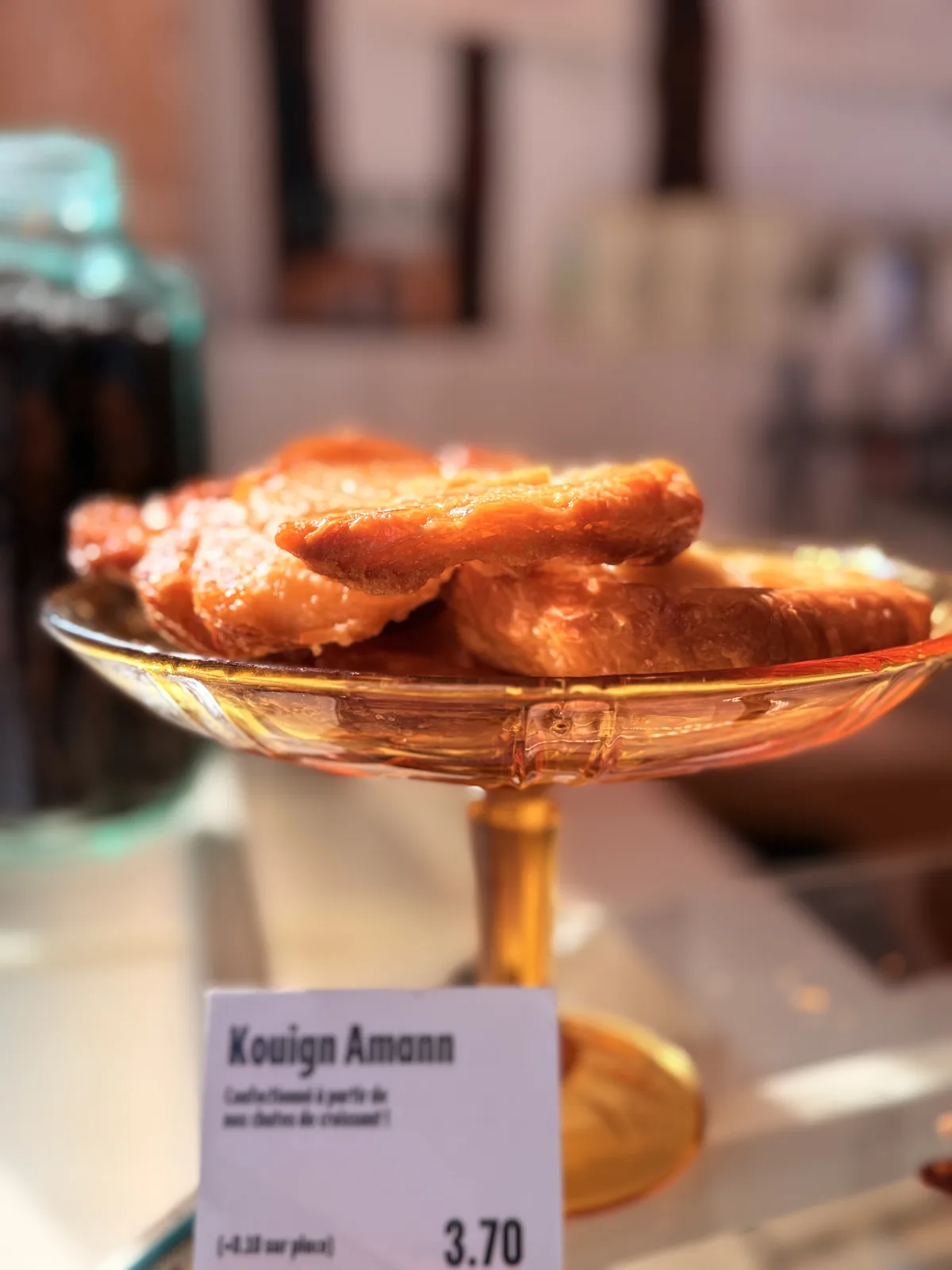 Kouign amann pastries on a footed glass stand in a Paris bakery window