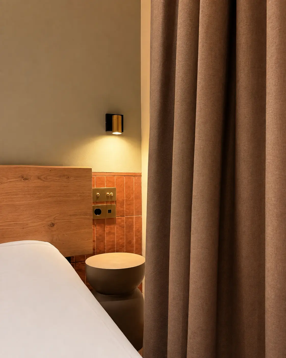 Linen curtain, bedside table and a lit terracotta wall in an Ambos Mundos guest room