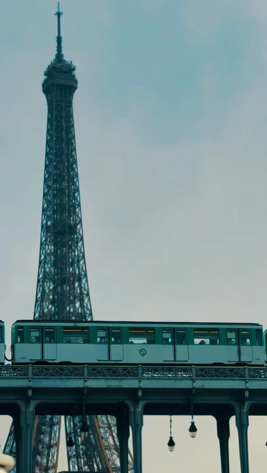 A teal Paris metro carriage crossing the viaduct with the Eiffel Tower behind