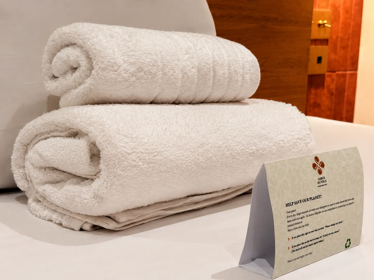 Rolled towels beside a printed sustainability card in an Ambos Mundos bathroom