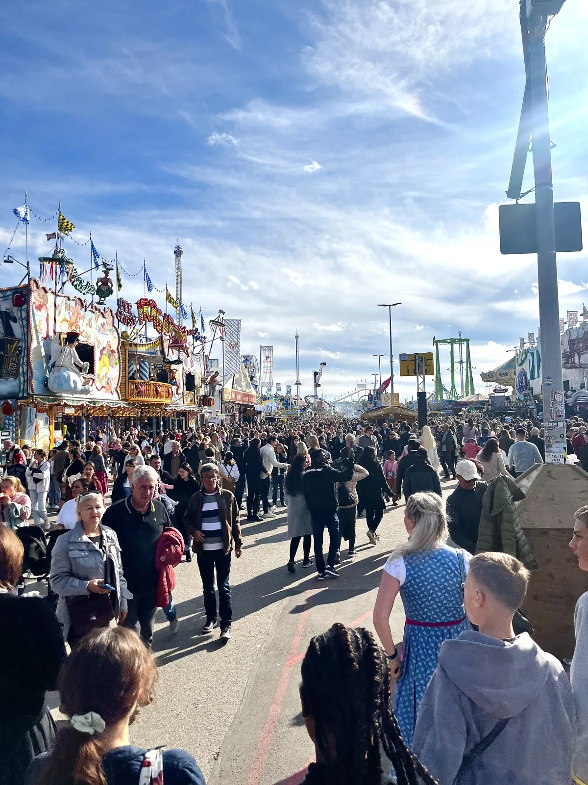 Crowds walking the fairground avenue at a Munich festival under a bright sky