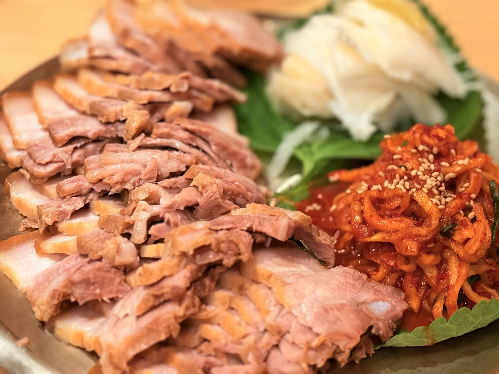 A platter of sliced pork bossam with kimchi and greens on a Seoul restaurant table